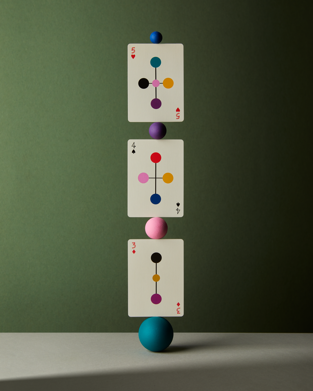 Three playing cards with colorful symbols balanced on a blue sphere against a green background