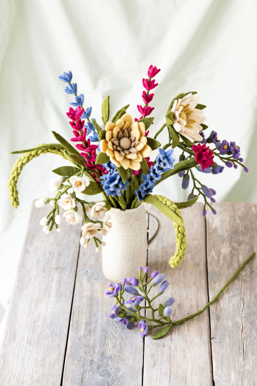 Felt flower bouquet in a mug on a wooden surface with a white background