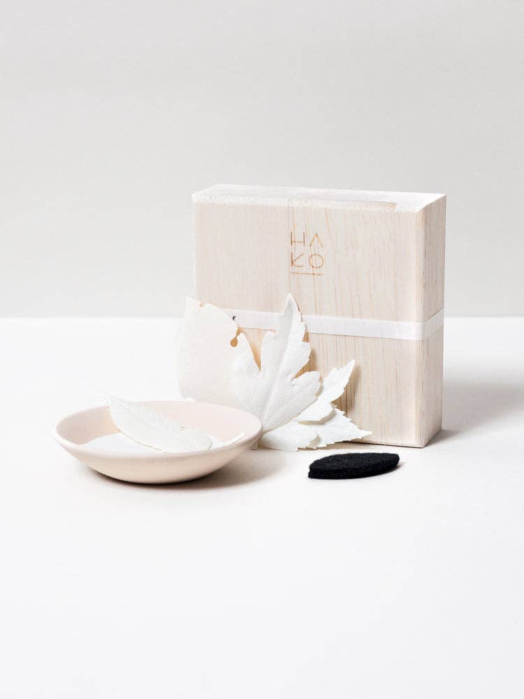 Paper incense leaves, small dish, and black mat on a white surface with a branded box.