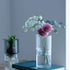 Clear vase with flowers on a blue book against a gray wall