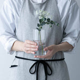 Person holding a clear vase with greenery against a neutral background