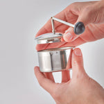 Hand holding a small metal tea infuser against a plain background