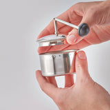 Hand holding a small metal tea infuser against a plain background