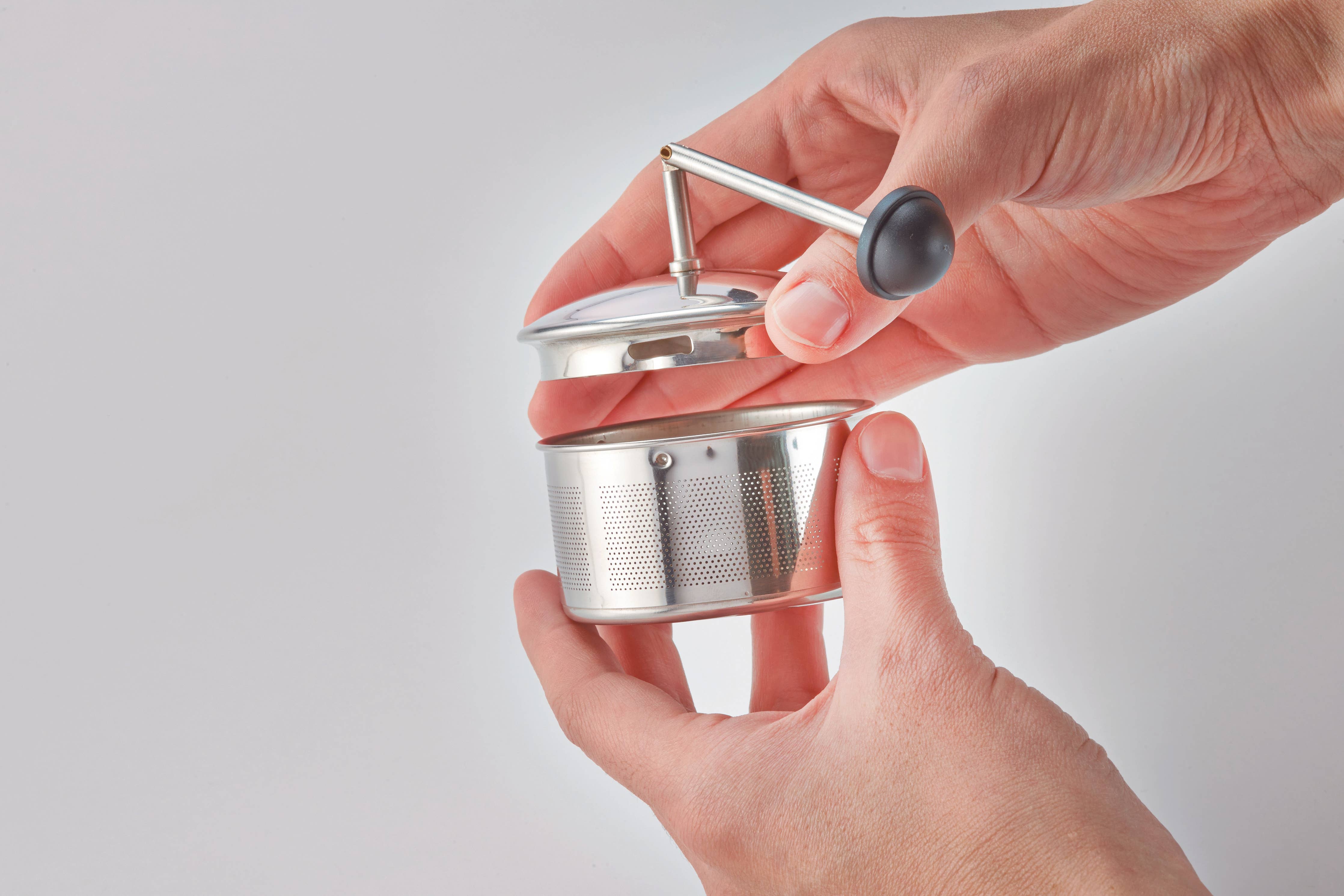Hand holding a small metal tea infuser against a plain background