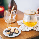 Person holding Teapot Strainer handle on a wooden table with cookies and a lit candle.