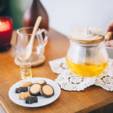 Person holding Teapot Strainer handle on a wooden table with cookies and a lit candle.
