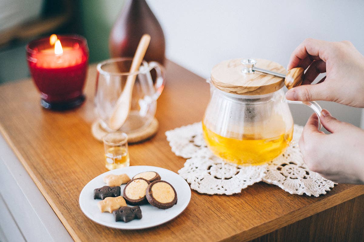 Person holding Teapot Strainer handle on a wooden table with cookies and a lit candle.