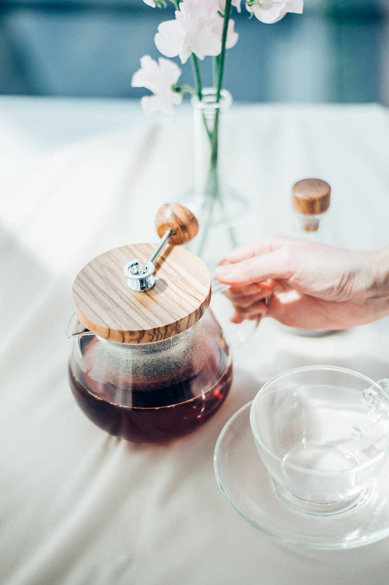 Glass teapot with wooden lid on a table with a blurred background