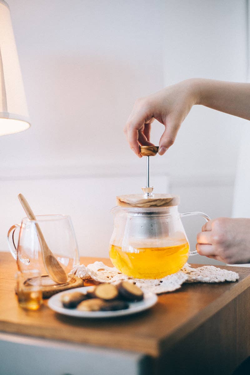 Person making tea with a teapot on a wooden table.