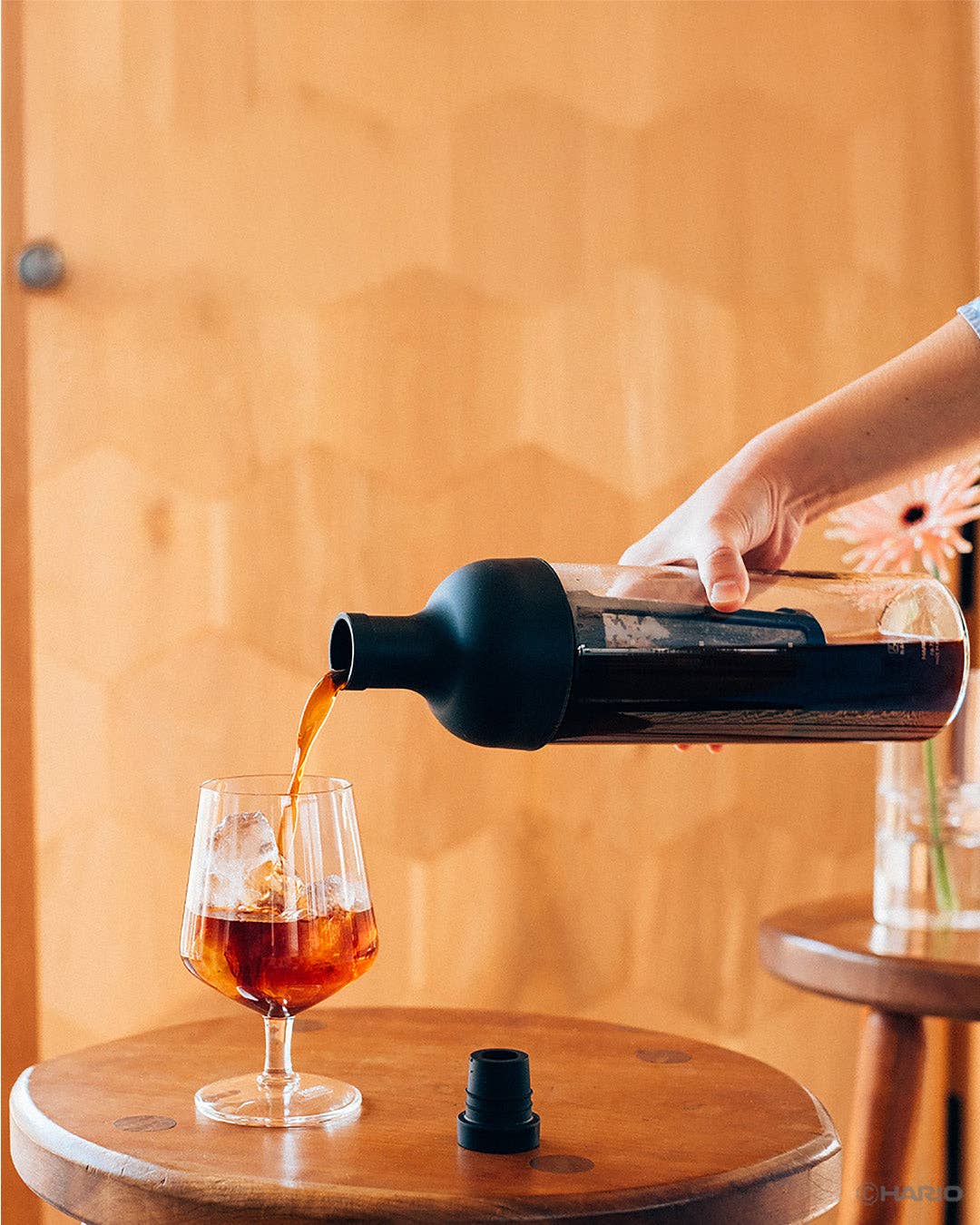 Person pouring dark liquid from a bottle into a glass on a wooden surface.