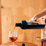 Person pouring dark liquid from a bottle into a glass on a wooden surface.