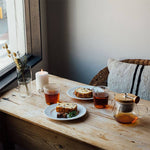 Pull up Teapot, tea cups, bread, and a candle on a wooden surface.