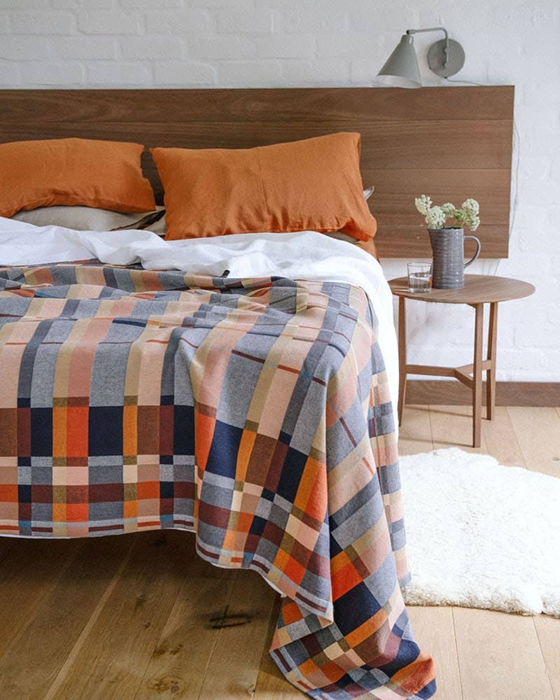 Bed with plaid blanket and orange pillows in a bedroom setting.