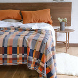 Bed with plaid blanket and orange pillows in a bedroom setting.