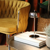 Yellow armchair next to a small round table with a lamp and books in a cozy room.