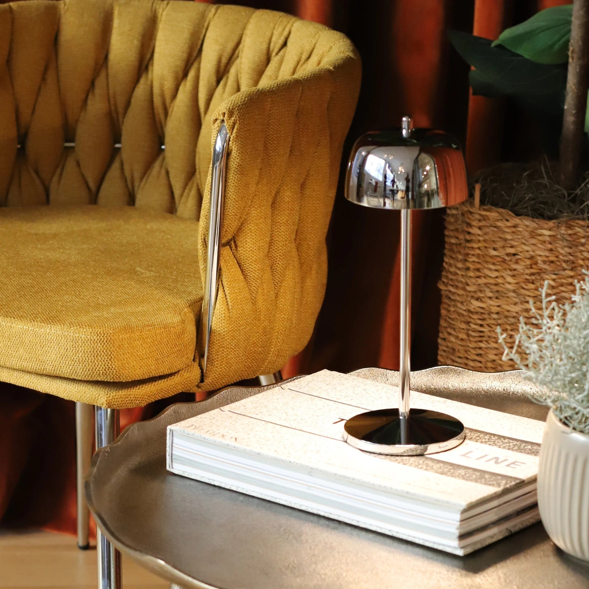 Yellow armchair next to a small round table with a lamp and books in a cozy room.