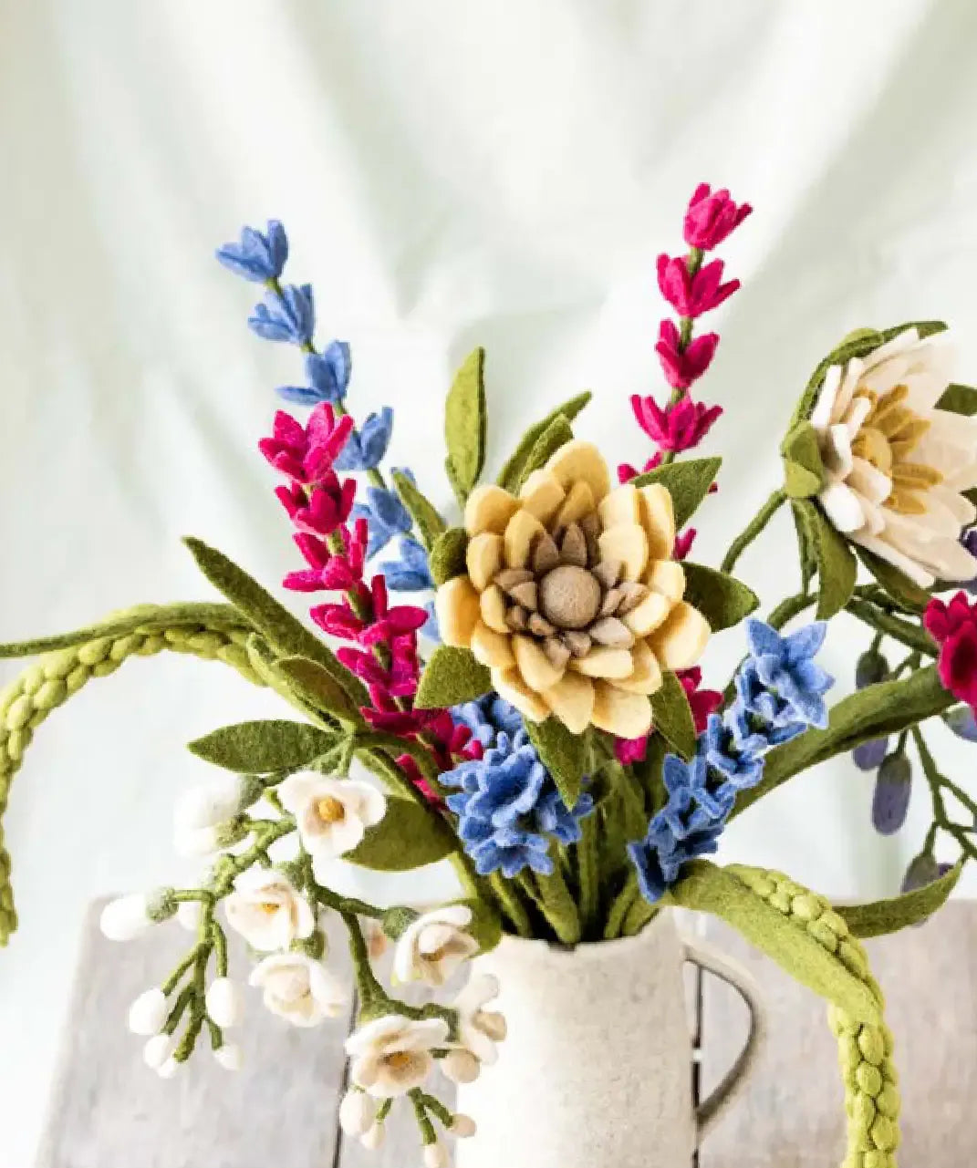 Colorful felt flower bouquet in a white vase on a light background.
