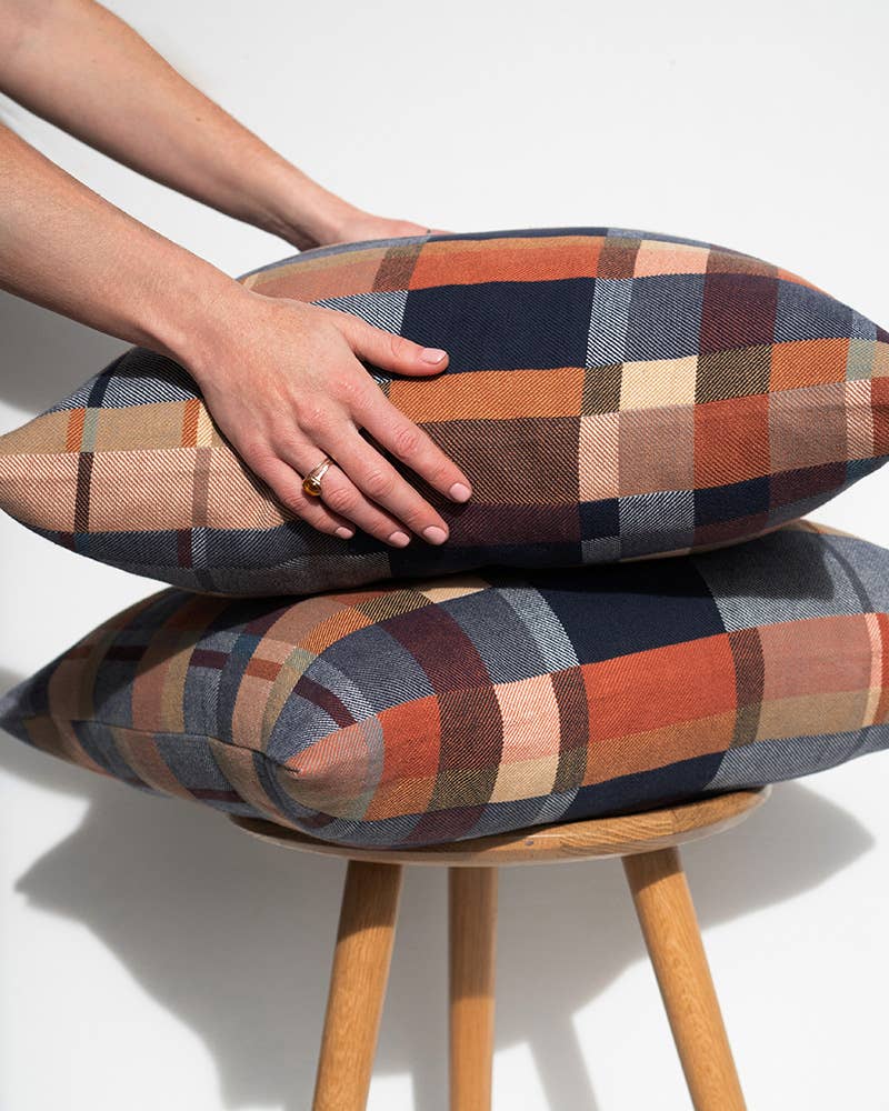 Stack of plaid patterned cushions on a wooden stool with a hand resting on top.