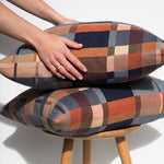 Stack of plaid patterned cushions on a wooden stool with a hand resting on top.