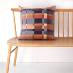 Plaid pillow on a wooden bench against a white background