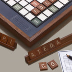 Wooden letter tiles  on racks and corner of board and scoring sheet on a beige surface.