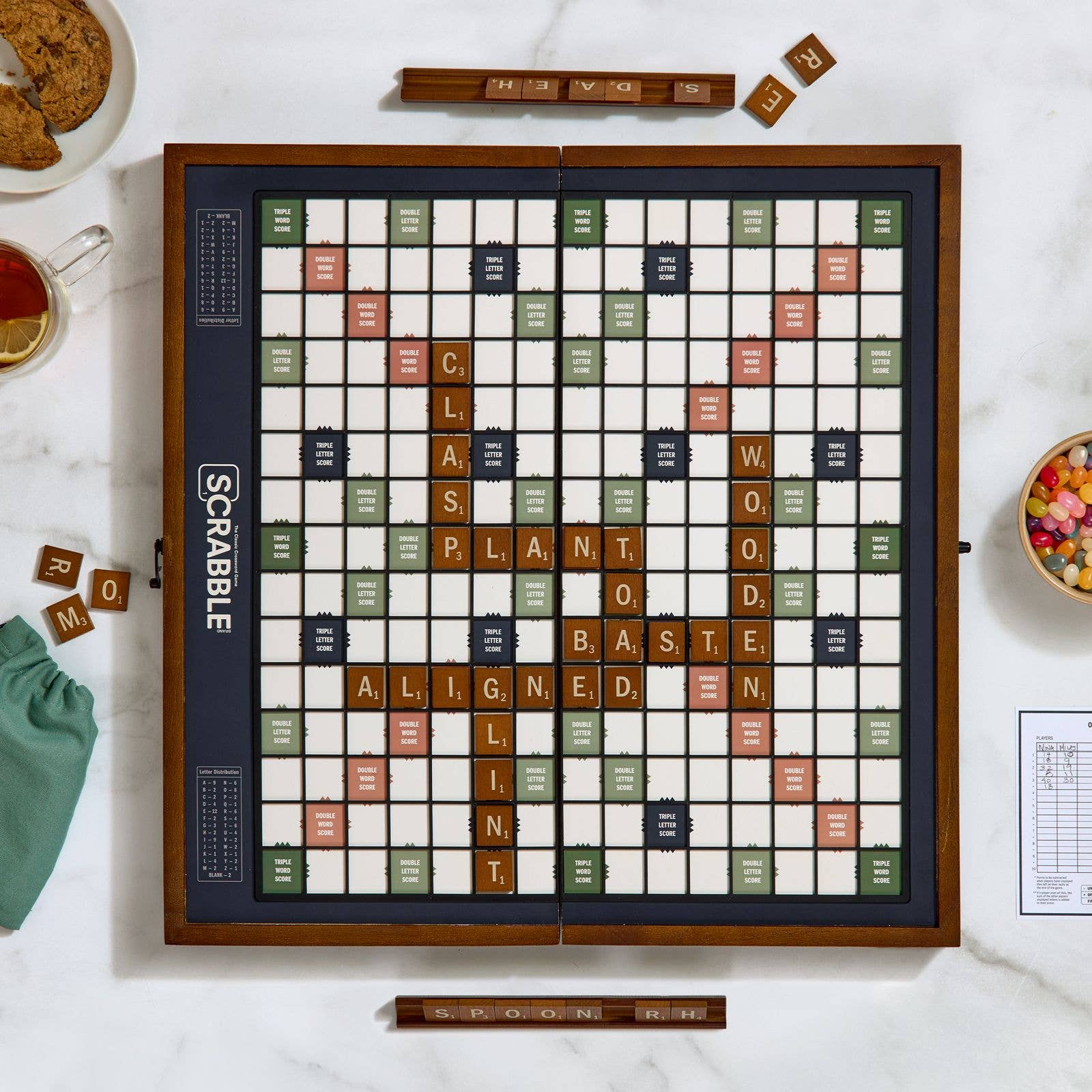 Scrabble board game on a table with tiles and food.