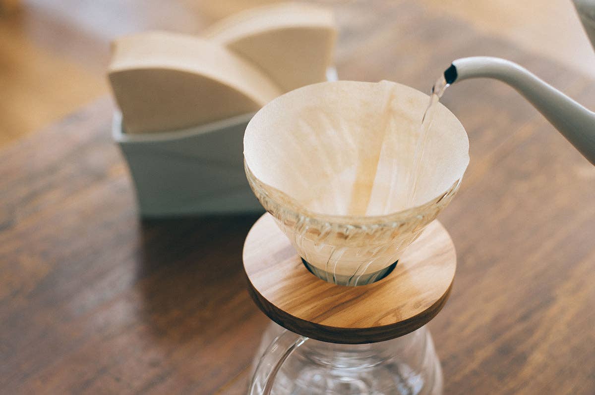 Water poured from kettle into coffee paper filter in glass drip coffee brew set on a wooden surface.