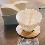 Water poured from kettle into coffee paper filter in glass drip coffee brew set on a wooden surface.