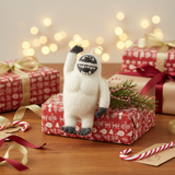 Plush abominable snowman ornament on a Christmas-themed gift box with festive decorations.
