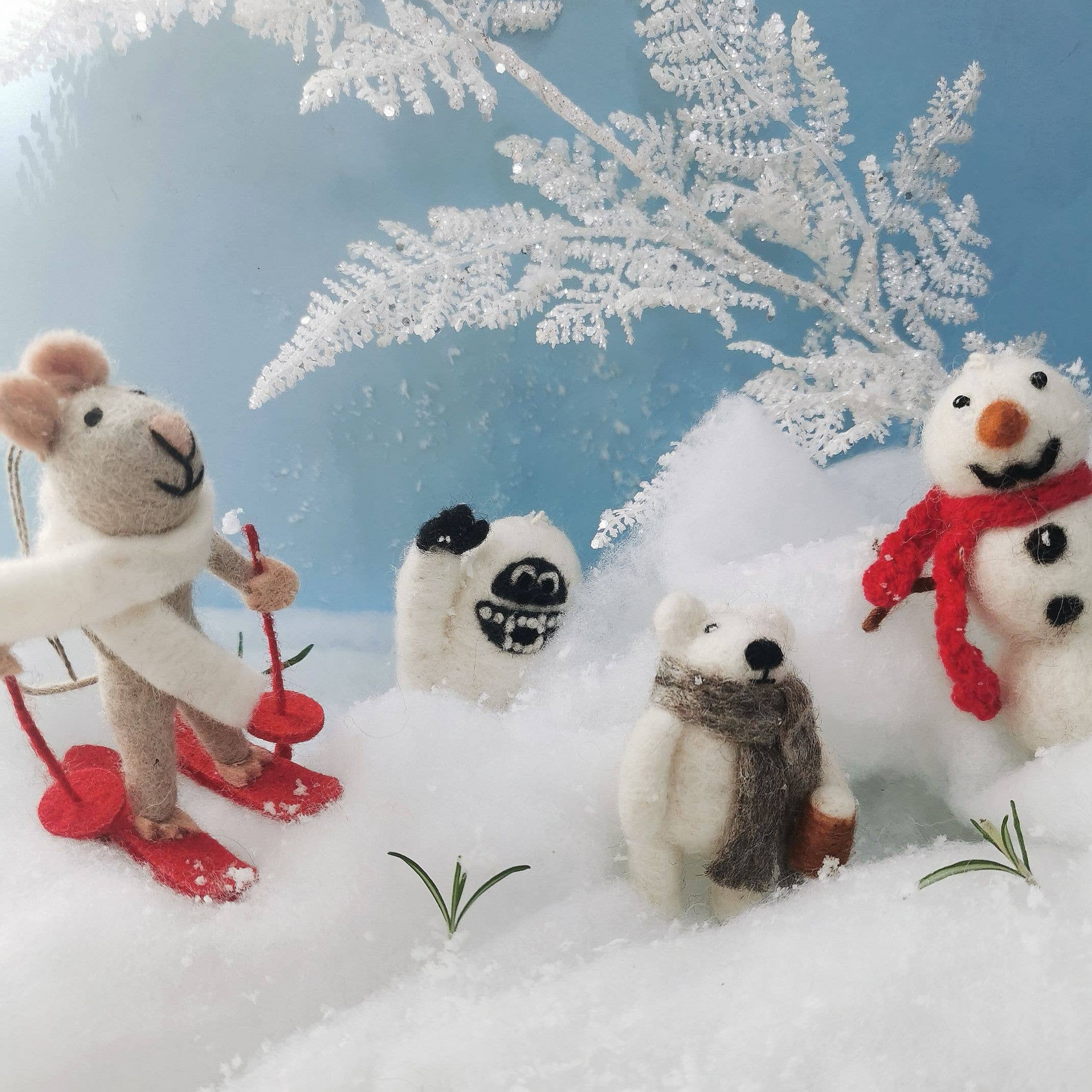 Toy mouse on skis, abominable snowman, polar bear, and snowman in a snowy scene with a blue sky.