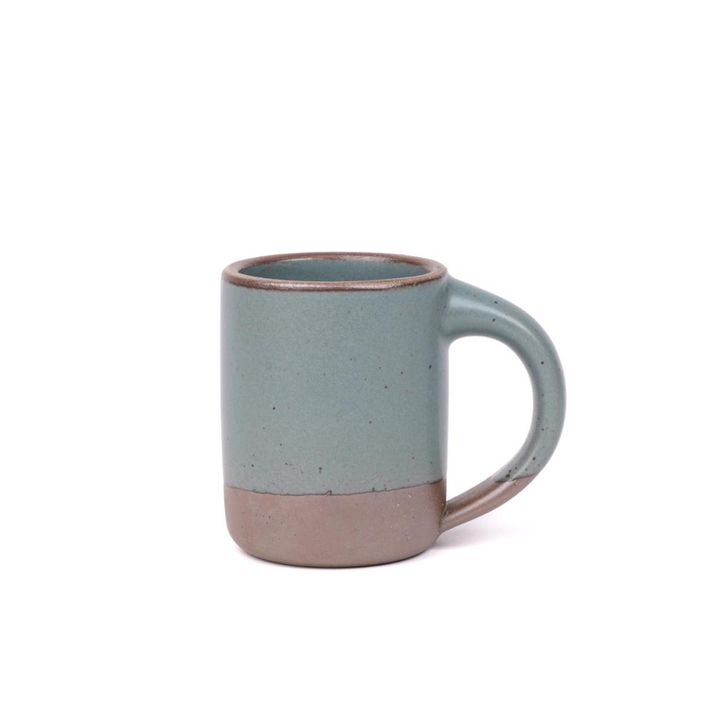 A medium sized ceramic mug with handle in a blue-grey color featuring iron speckles and unglazed rim.