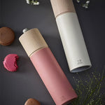 Salt and pepper grinders with wooden tops in dark pink and white laying on its side on a dark surface with cookies and flowers.