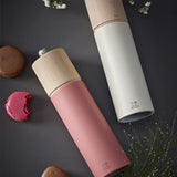 Salt and pepper grinders with wooden tops in dark pink and white laying on its side on a dark surface with cookies and flowers.