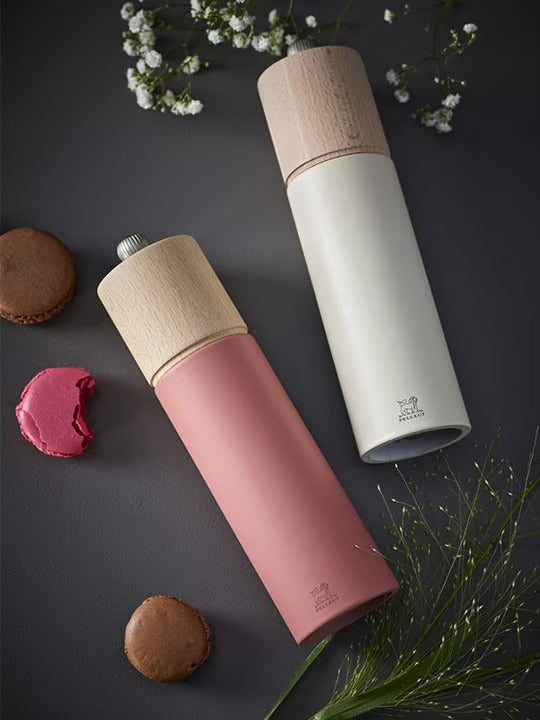 Salt and pepper grinders with wooden tops in dark pink and white laying on its side on a dark surface with cookies and flowers.