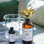 Large bottle with funnel, small bottle, and measuring cup on a marble surface with a couch in the background.