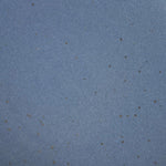 A closeup of a ceramic plate in a cool medium blue color with iron speckles throughout