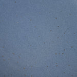 A closeup of a ceramic plate in a cool medium blue color with iron speckles throughout