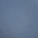 A closeup of a ceramic plate in a cool medium blue color with iron speckles throughout