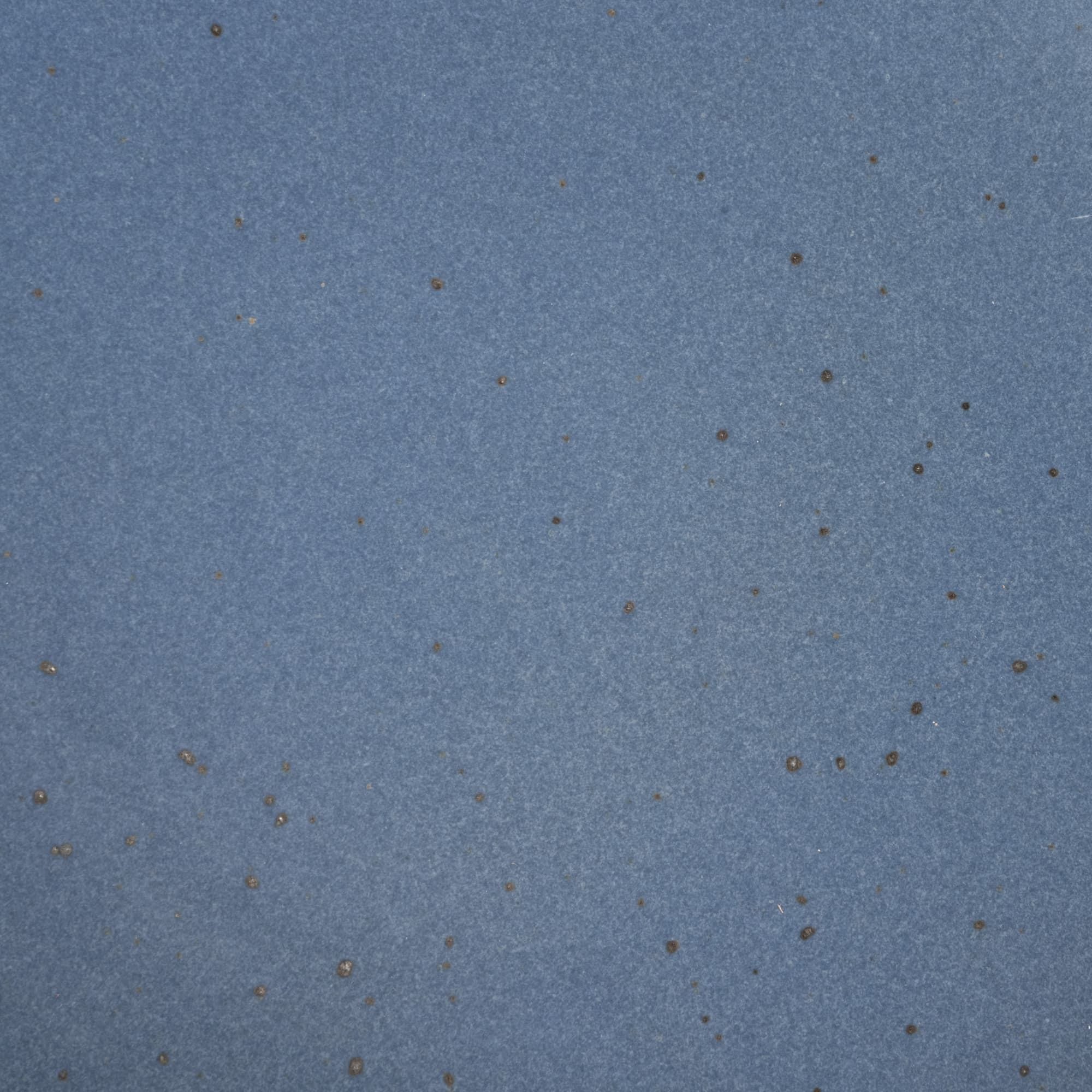 A closeup of a ceramic plate in a cool medium blue color with iron speckles throughout