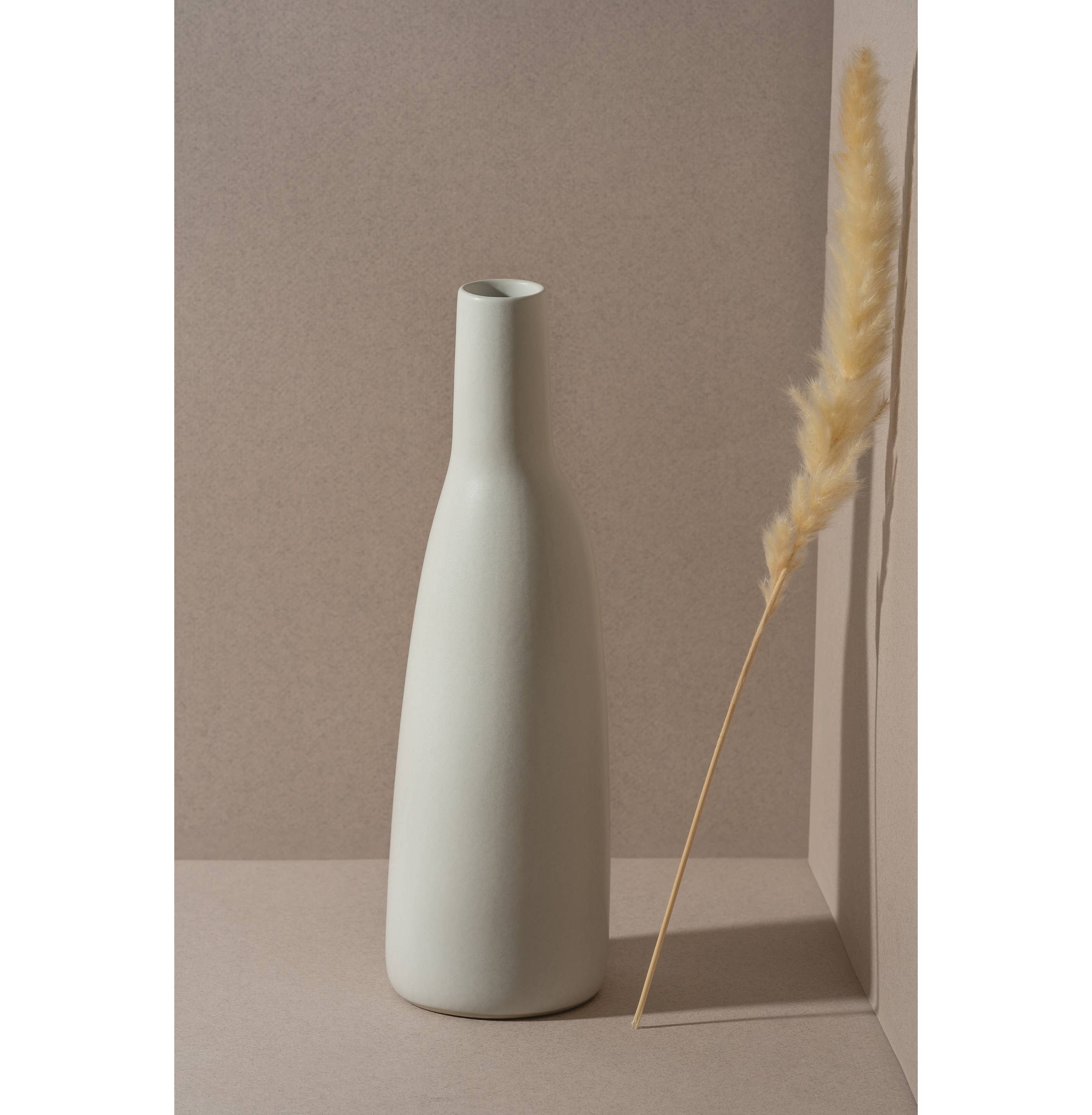 White vase on a neutral background with a dried plant