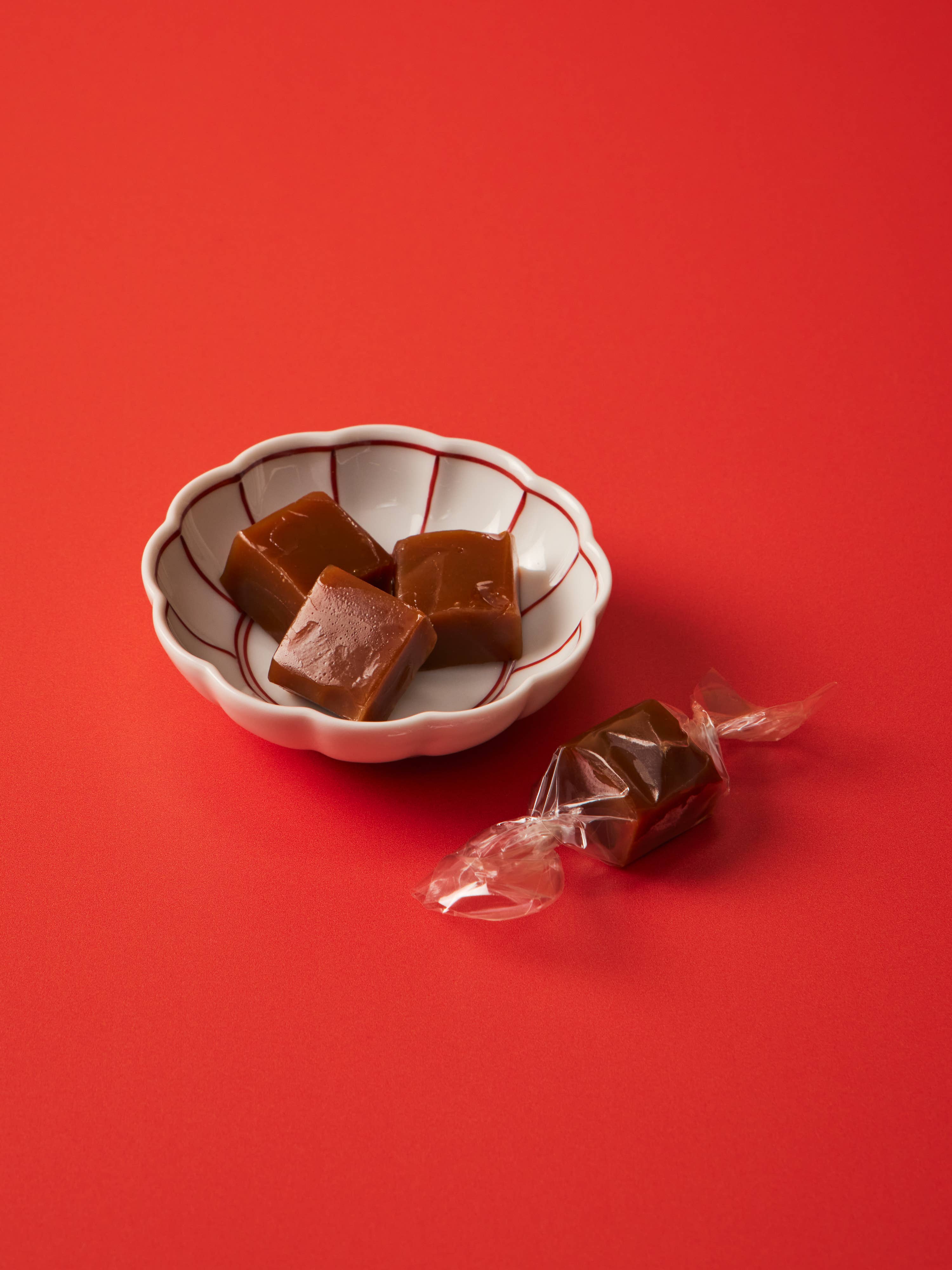 Small white bowl with brown candies on a red background