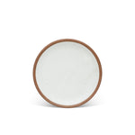 A medium sized ceramic plate in a cool white color featuring iron speckles and an unglazed rim.
