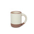 A medium sized ceramic mug with handle in a warm, tan-toned, off-white color featuring iron speckles and unglazed rim and bottom base.