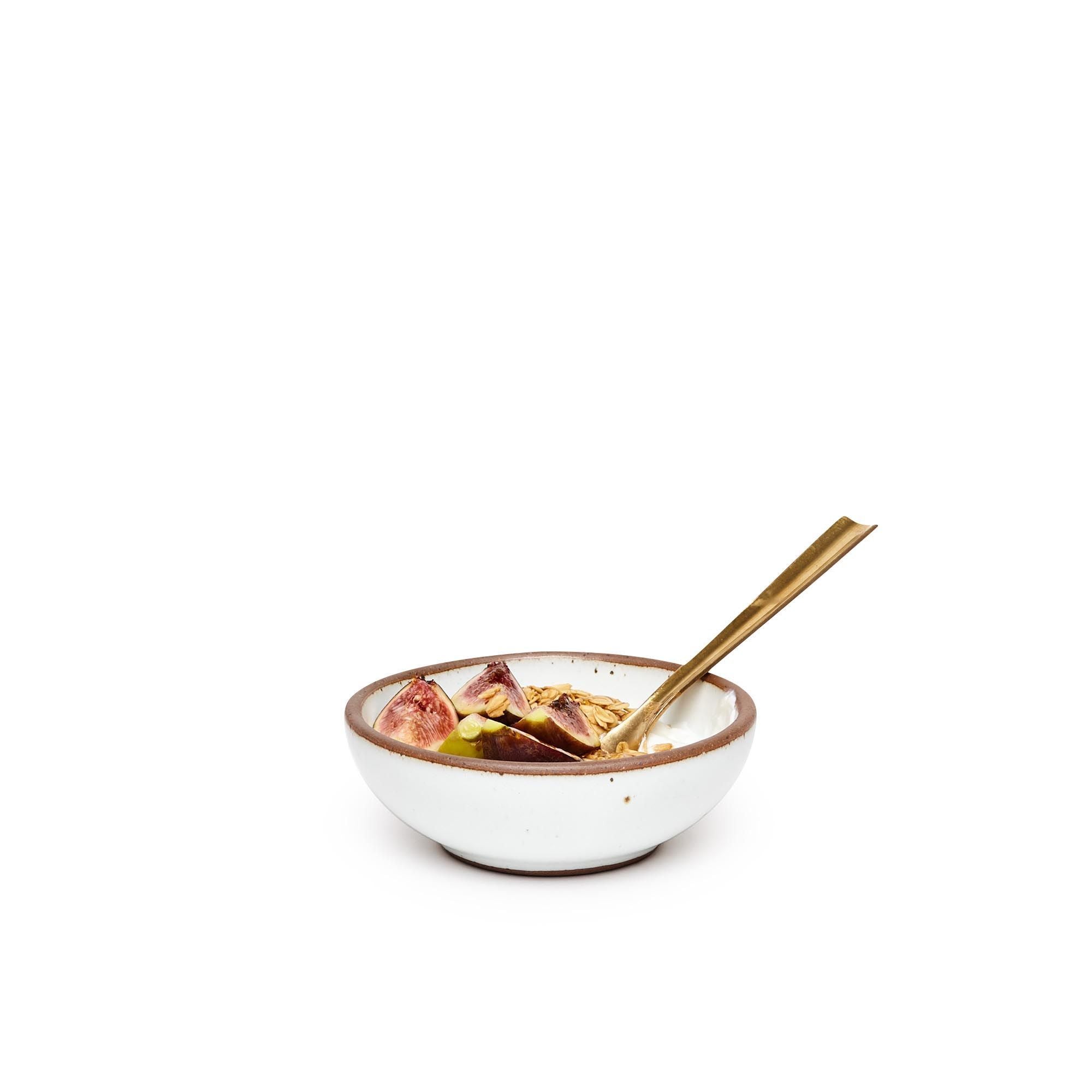 Yogurt and fruit with spoon in a small shallow ceramic bowl in a cool white color featuring iron speckles and an unglazed rim