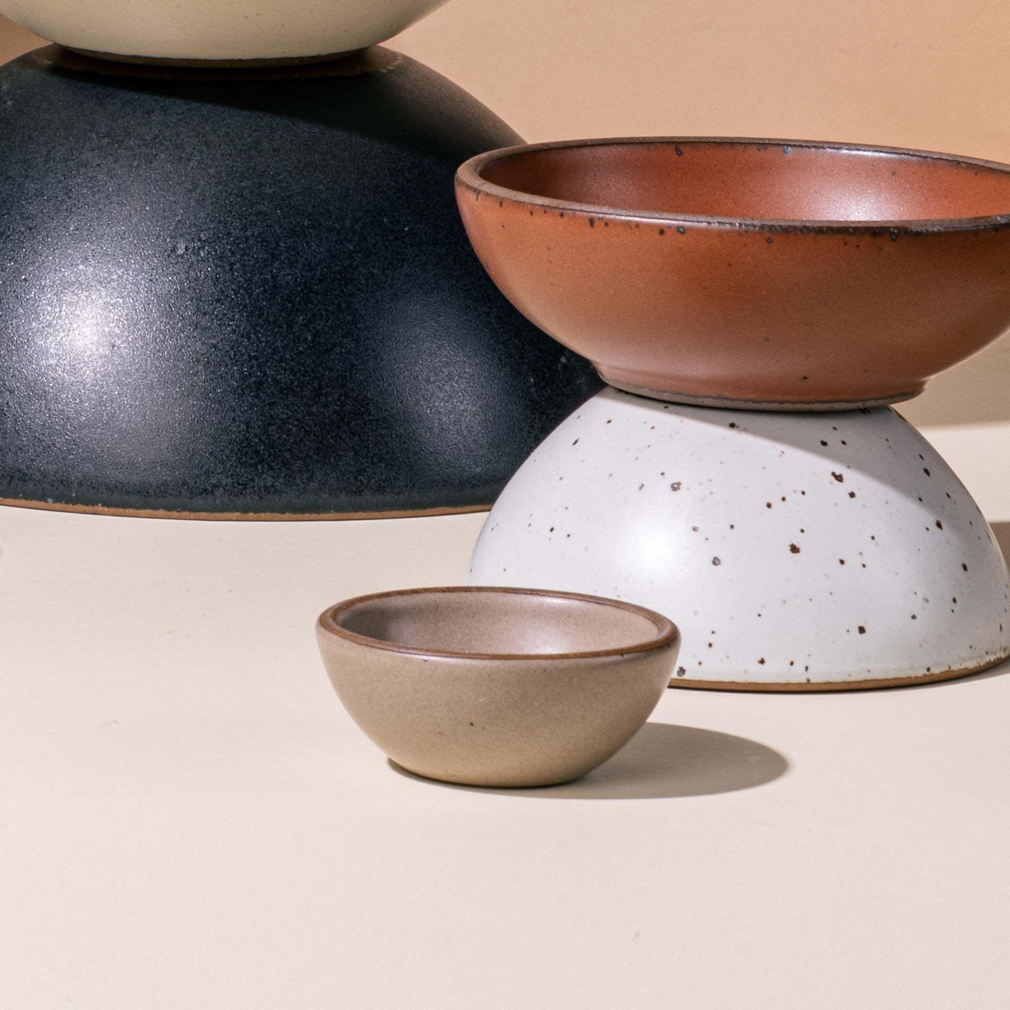 A tiny ceramic bowl in a muted tan color sits next to larger ceramic bowls in terracotta and white colors.
