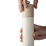 White salt grinder with wooden top held by a hand on a white background