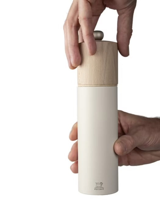 White salt grinder with wooden top held by a hand on a white background