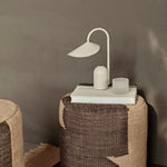 Woven side table with a lamp and book against a neutral wall