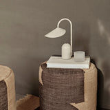 Woven side table with a lamp and book against a neutral wall