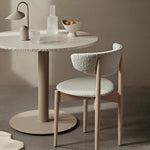 Round marble table with lamp and glassware and chair in a neutral minimalist setting.